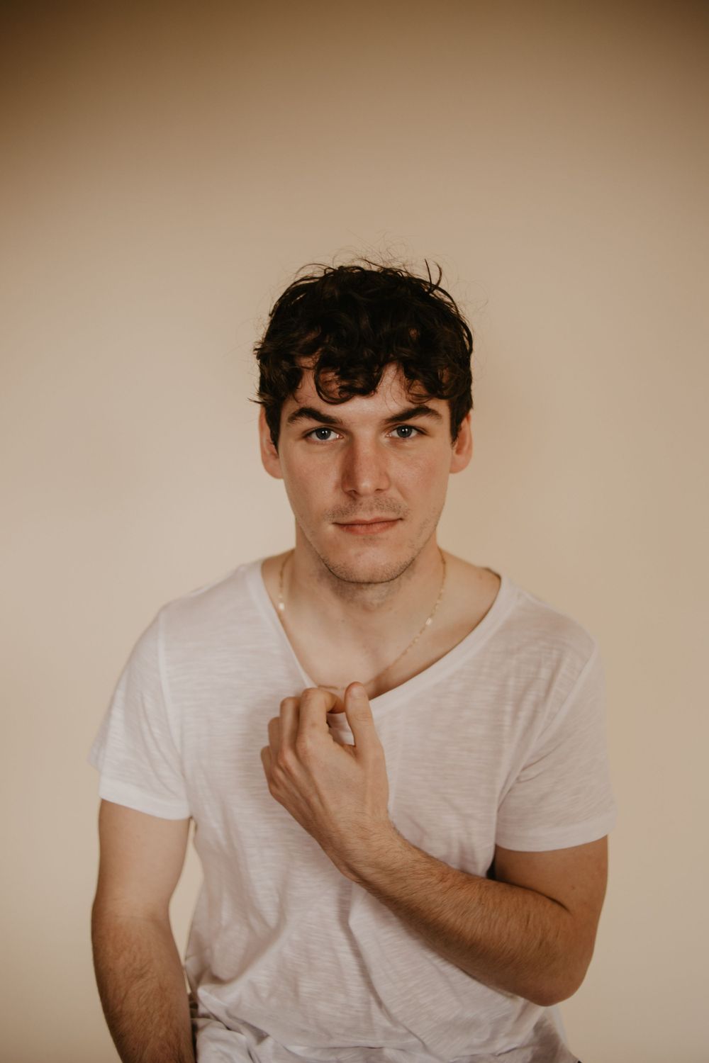 Portrait of person in white t-shirt against beige wall with natural lighting.