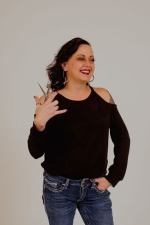 Person in black top and jeans strikes fun pose against light studio background.