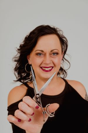 Person displays scissors while wearing black top and silver hoop earrings.