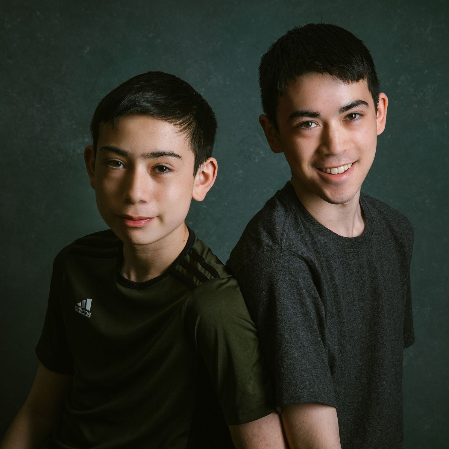 Two young boys pose for a portrait against a dark textured background.