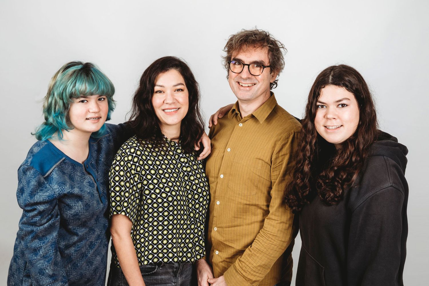 A group of four people posing together against a white backdrop.