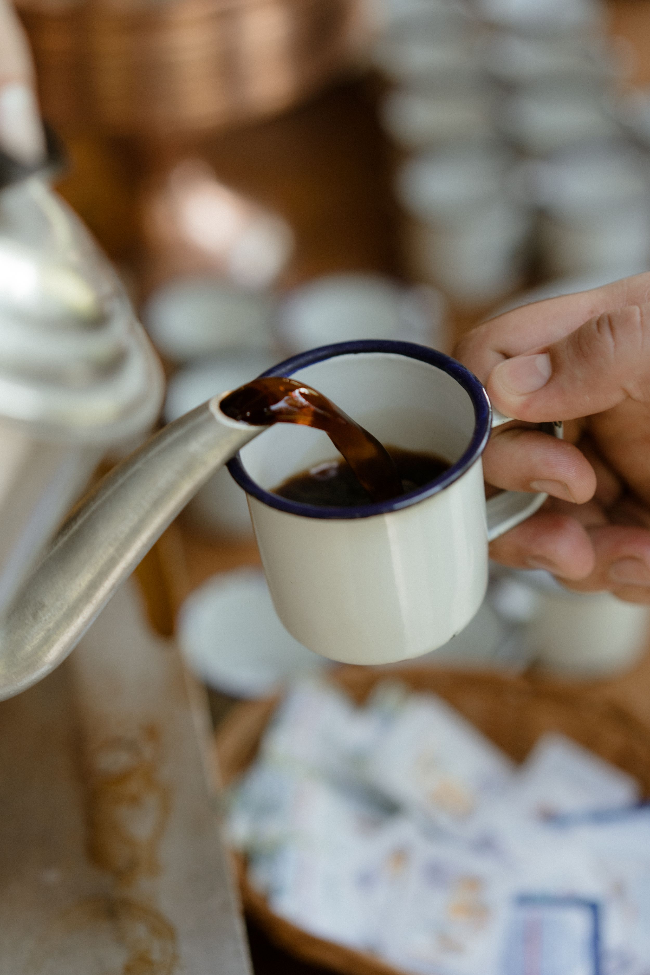 Hands pouring dark liquid from ceramic pitcher into cups.