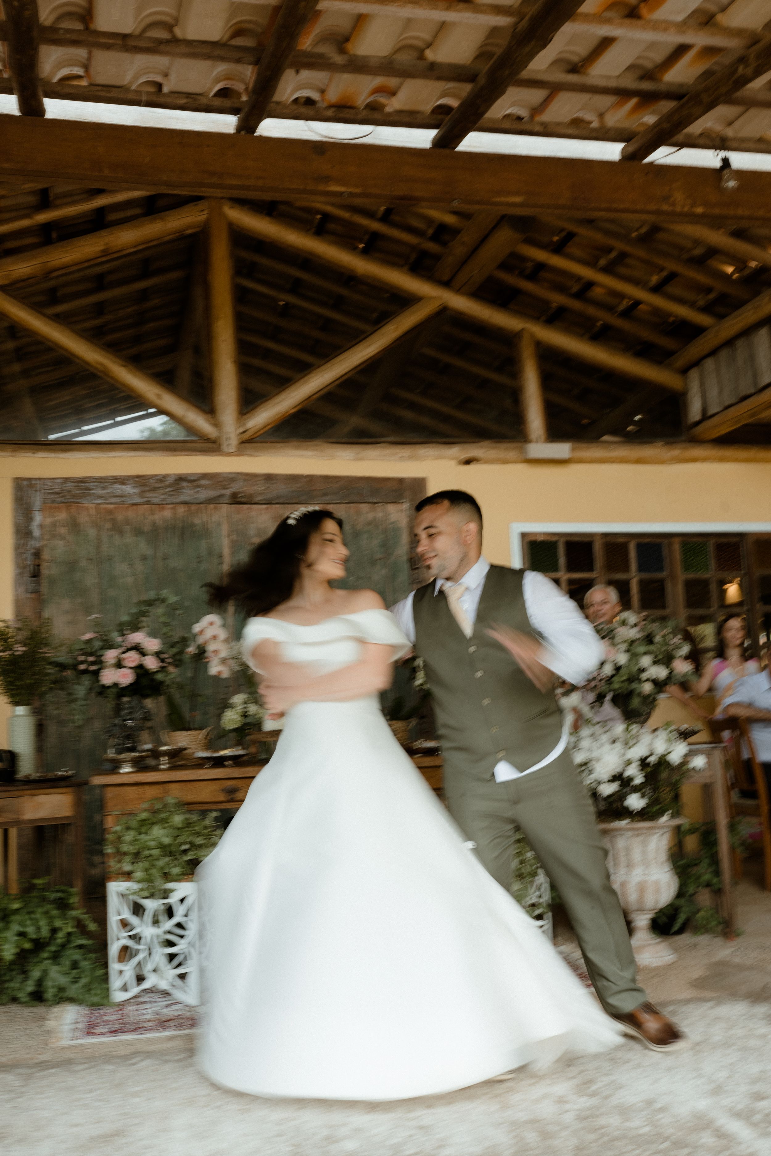 Wedding couple dances under rustic wooden beamed ceiling with floral decorations.