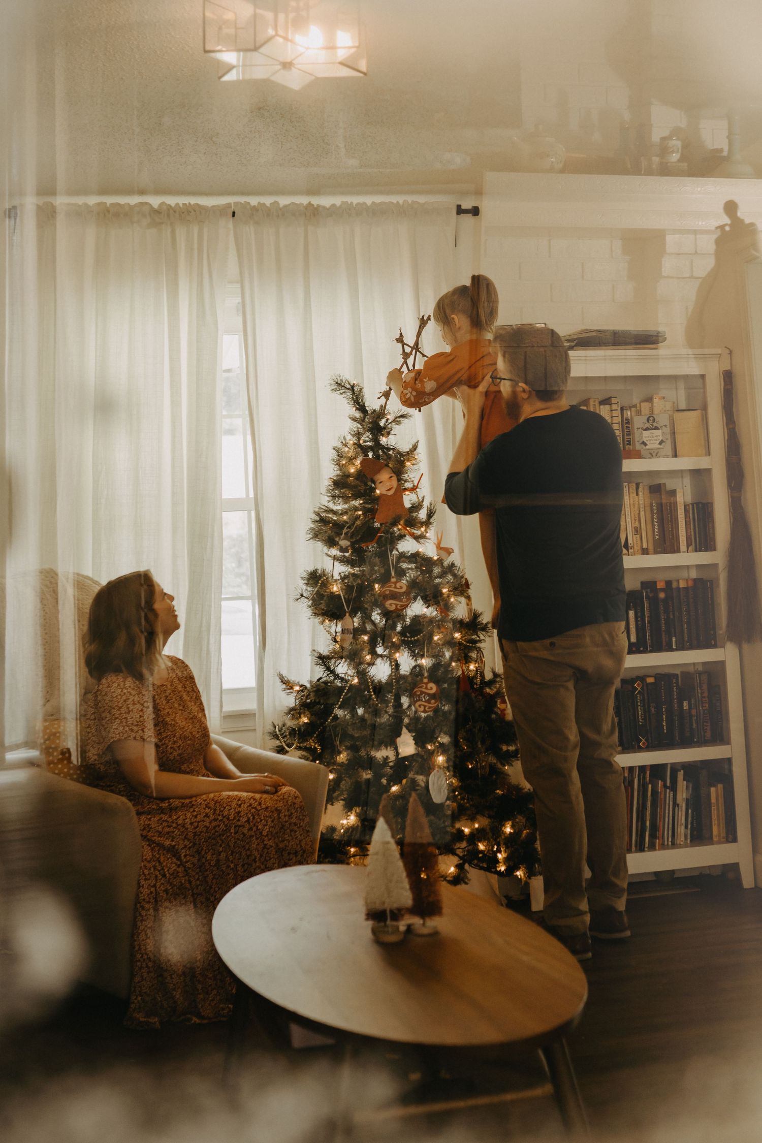 Family decorates a Christmas tree together in a cozy living room with warm holiday lighting.