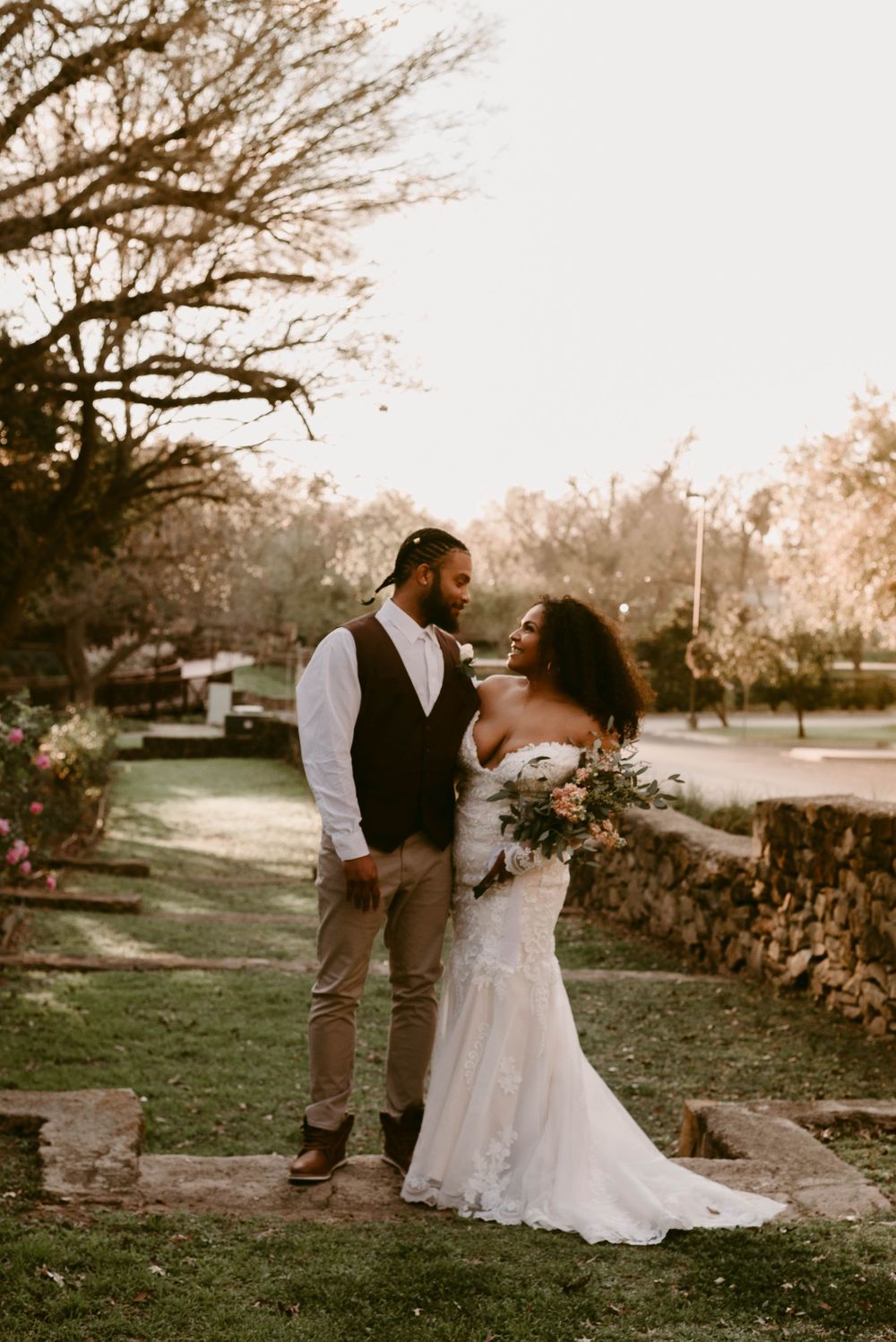 A romantic sunset wedding photo of a couple embracing on landscaped grounds.