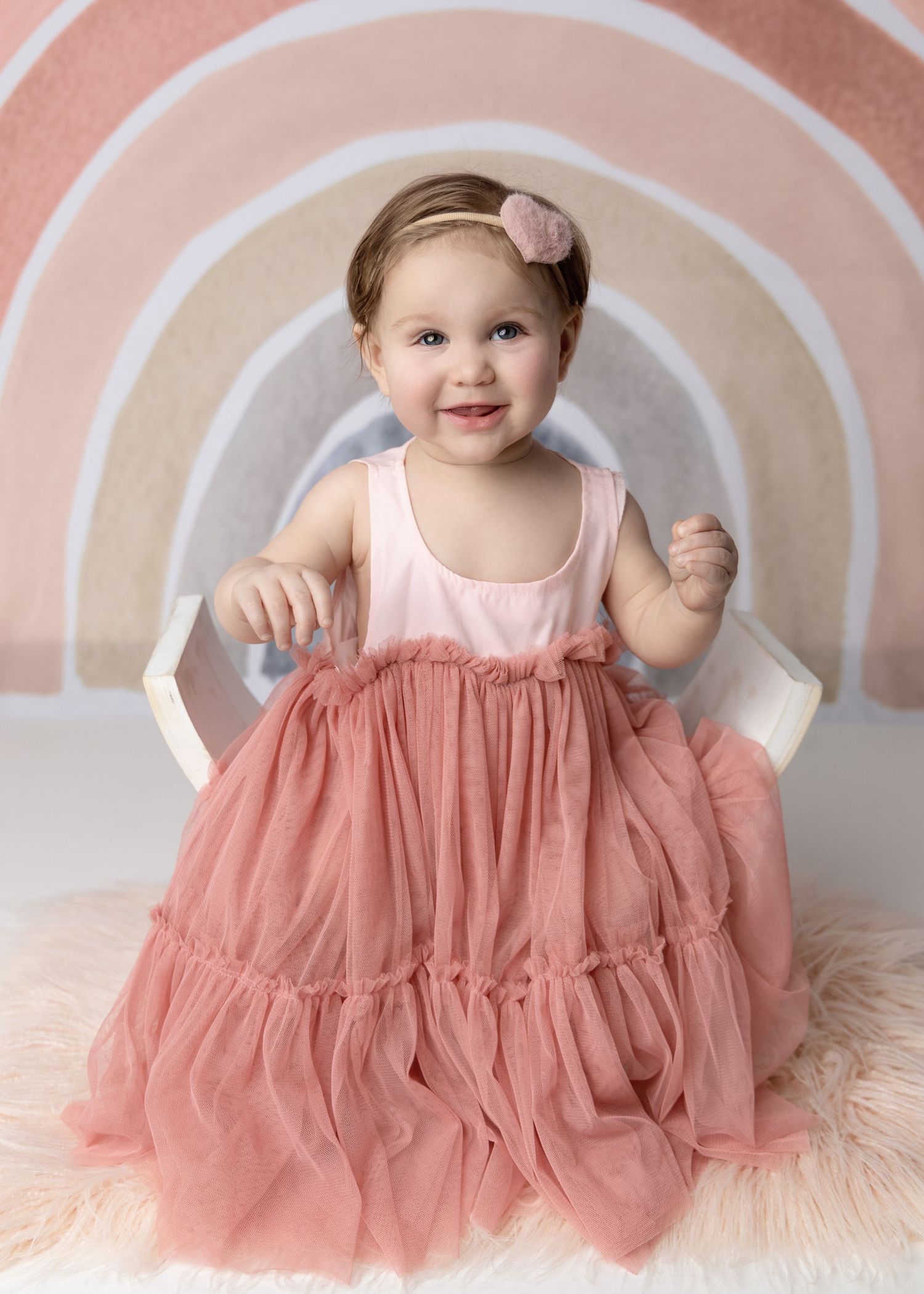 Baby in pink tulle dress against pastel rainbow backdrop.