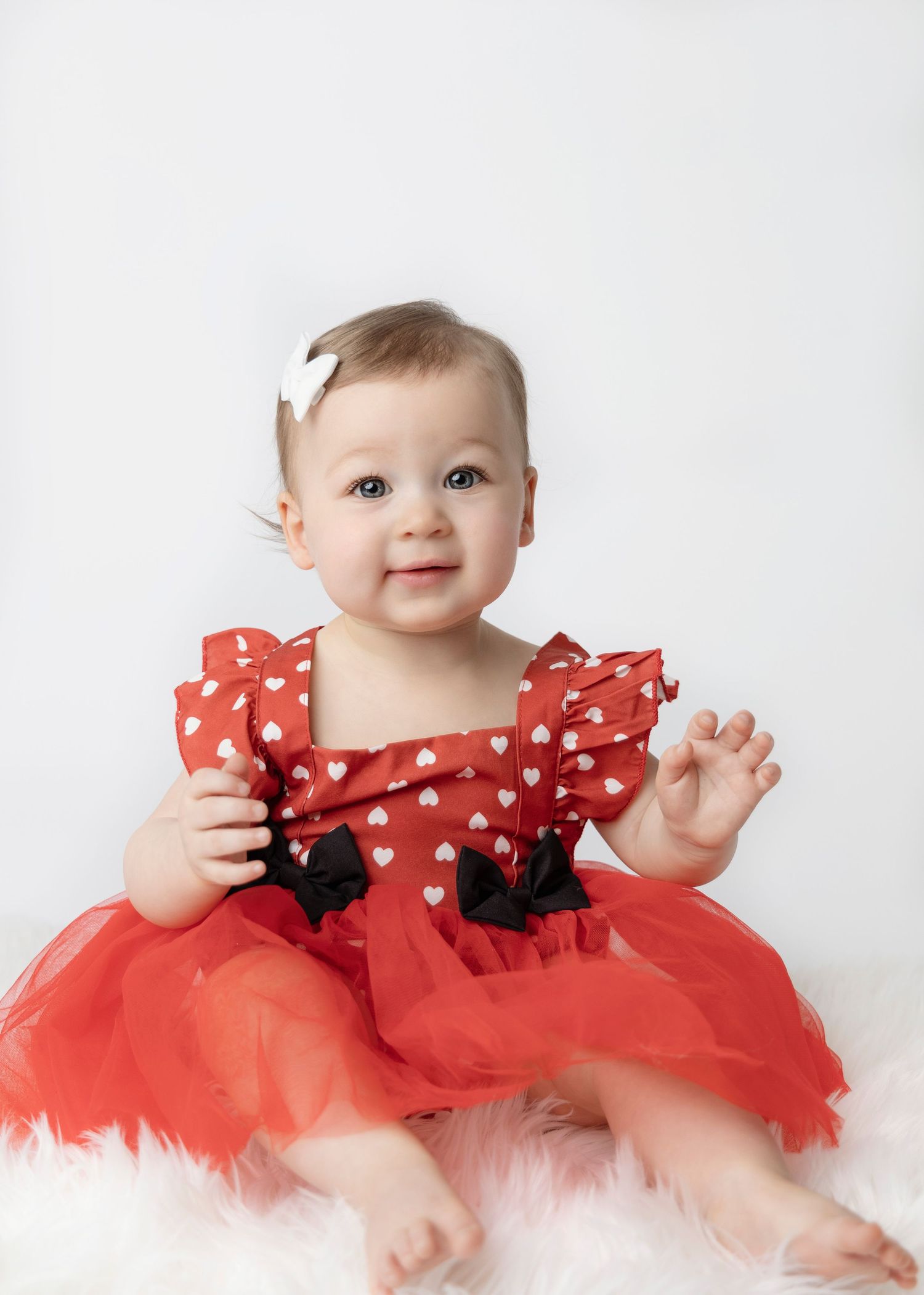 Baby wearing red polka dot dress with tulle skirt and white bow accessory.