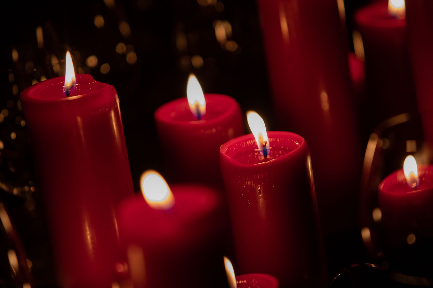 Several lit red pillar candles glowing warmly against a dark background with soft bokeh lights.