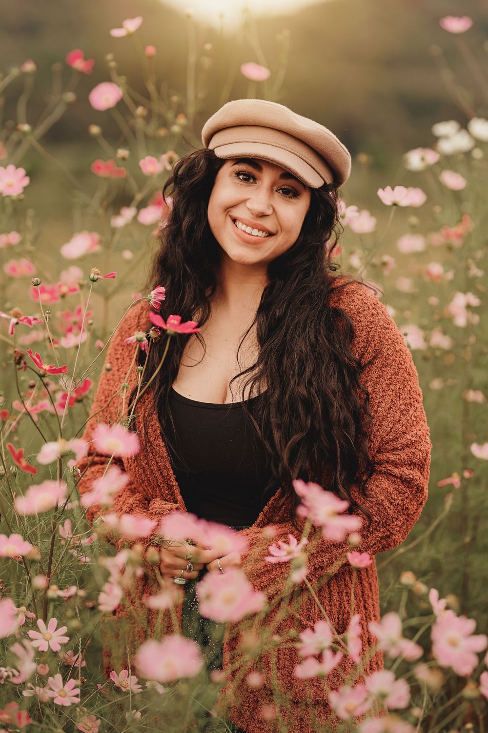 Portrait in wildflower field with pink cosmos flowers and warm sunset lighting.