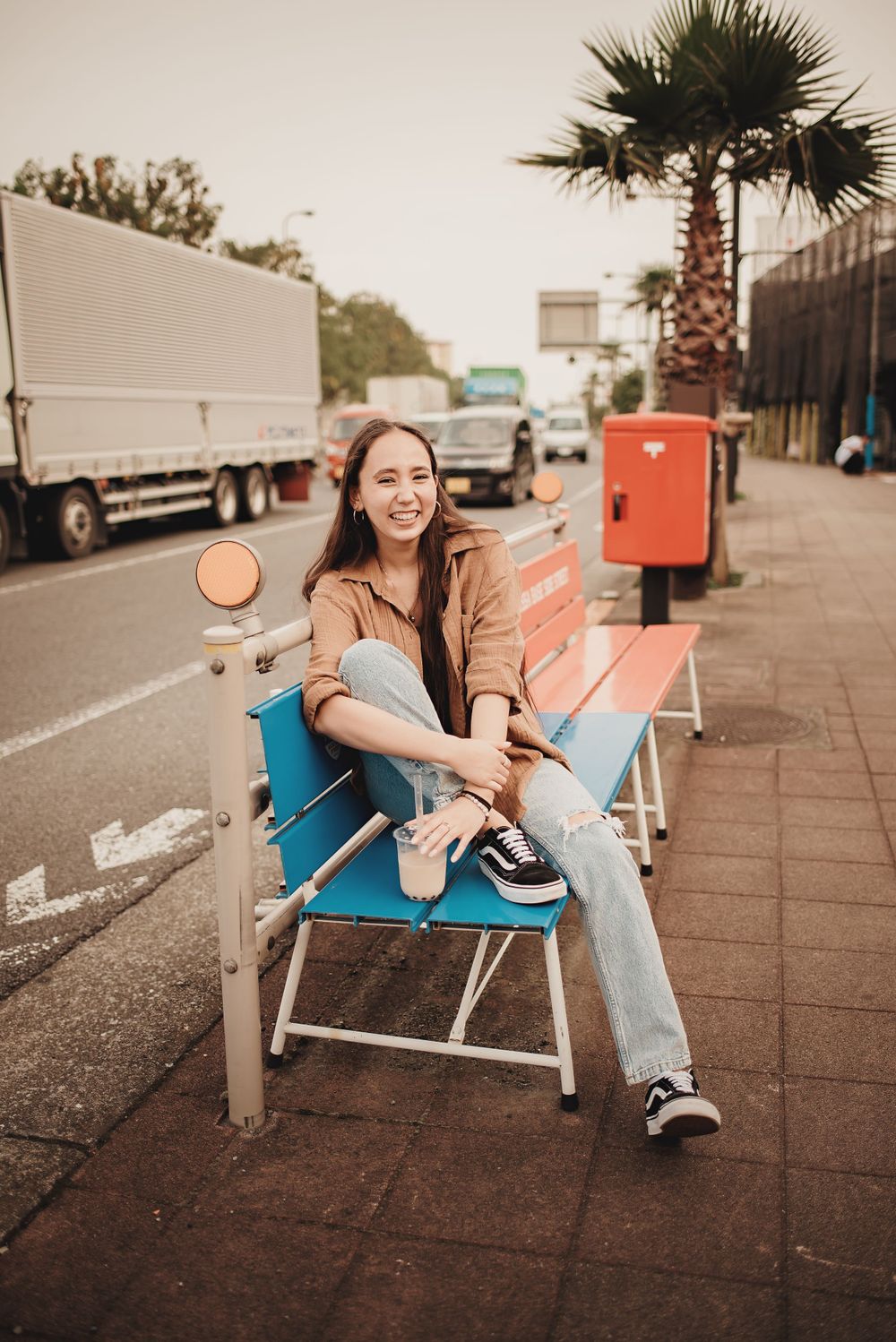 Candid lifestyle photo on a blue bench near a palm tree and parked truck.