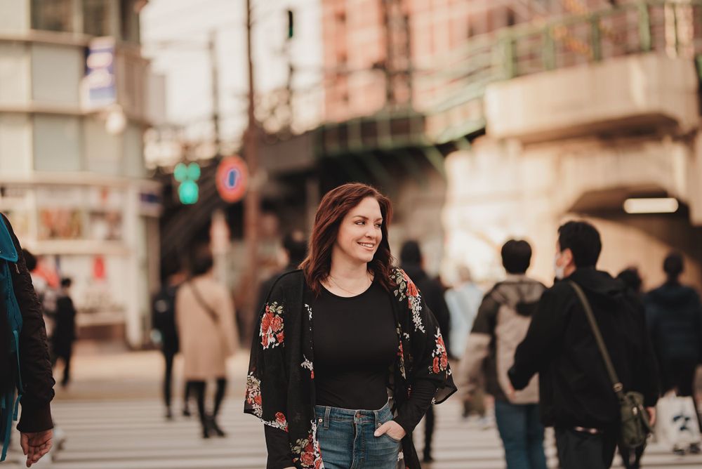 Stylish person walking on a busy urban street wearing a black top and jeans at sunset.