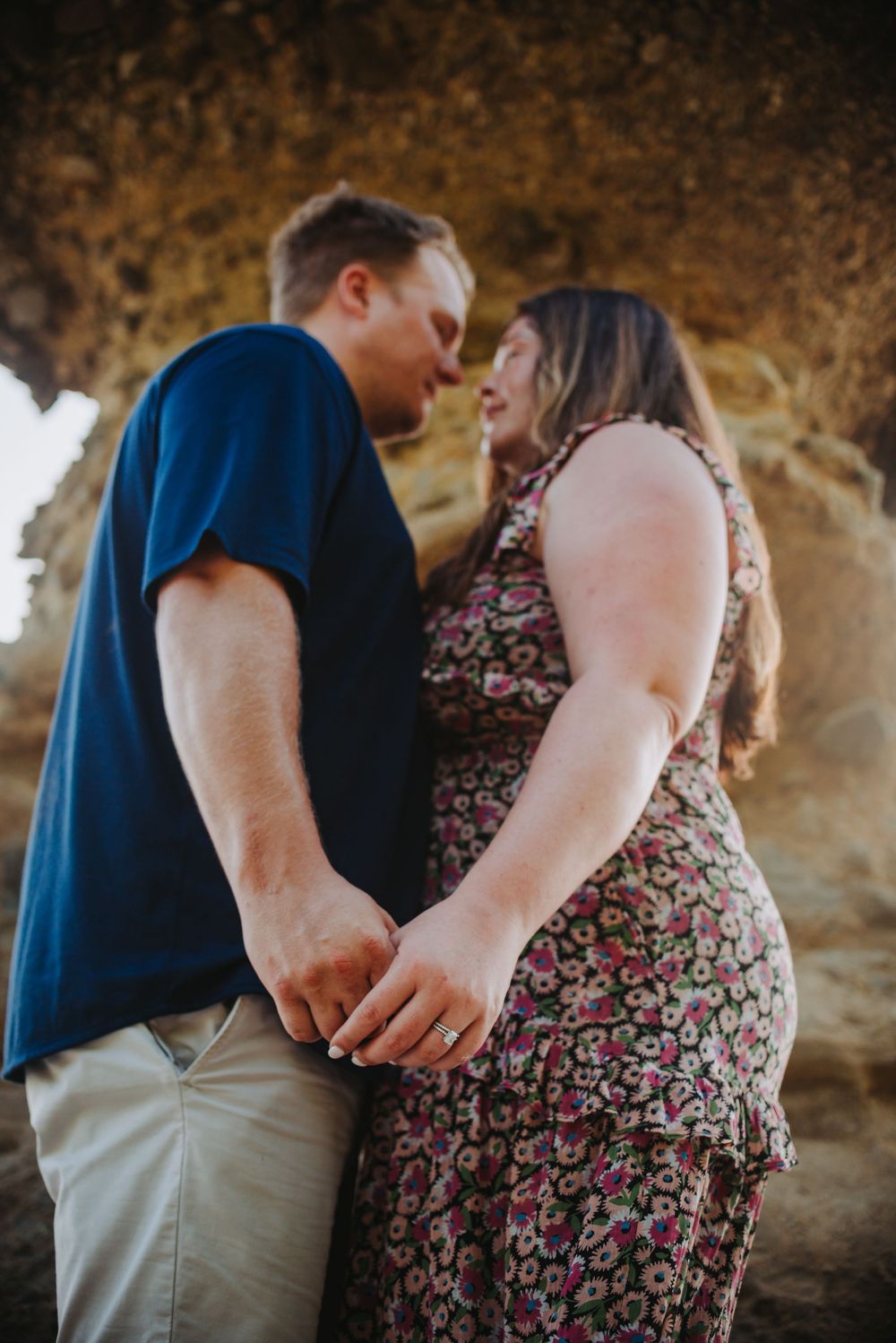 A romantic couple shares a tender moment in front of a rocky background during a sunset photoshoot.
