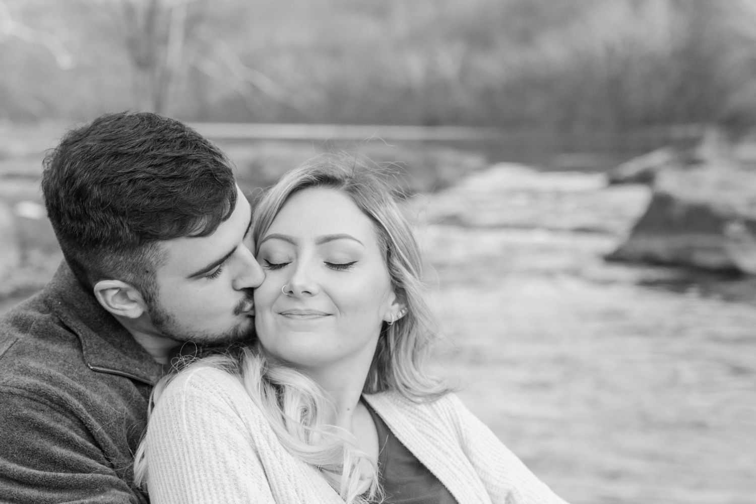 A tender black and white portrait of a couple sharing an intimate moment by a river.