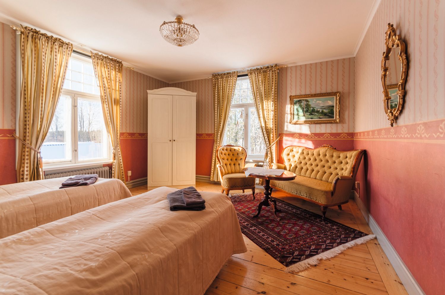 Elegant hotel room with twin beds, vintage decor, yellow curtains, and antique furniture on hardwood floors.