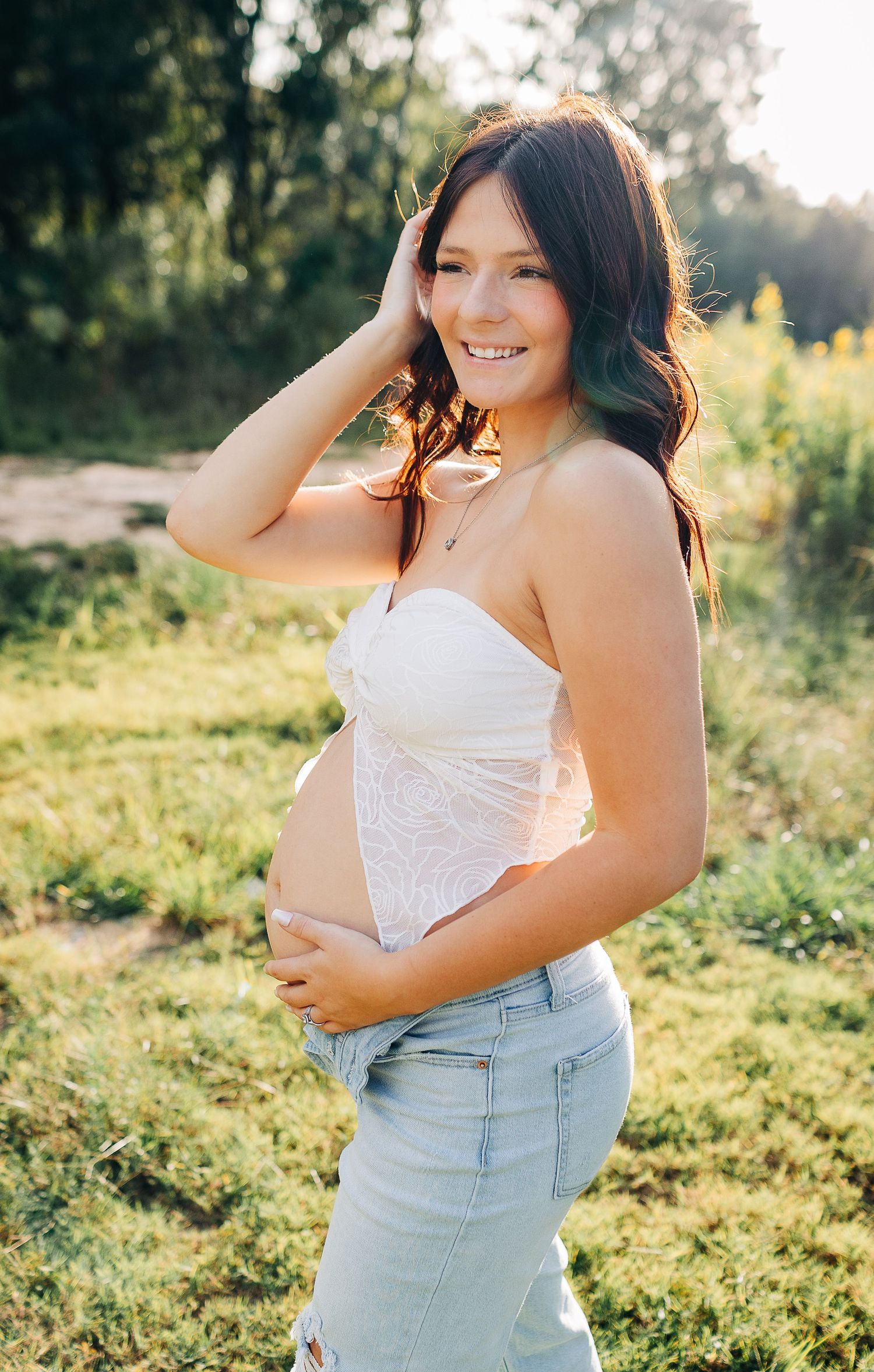Woman in white top and light denim poses in sunny field during golden hour portrait session in destin Florida o