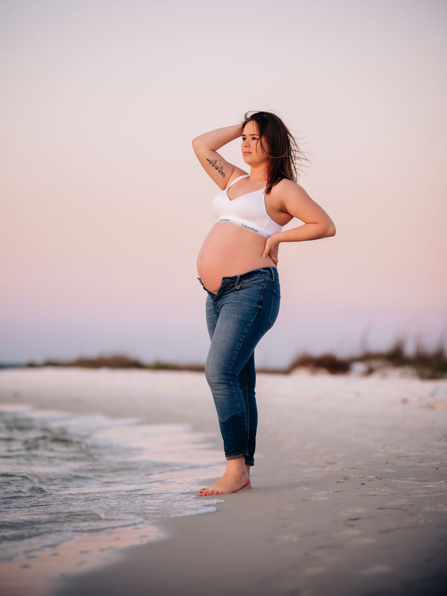 Silhouetted figure creates artistic maternity portraits along peaceful beach shoreline at sunset at destin Florida