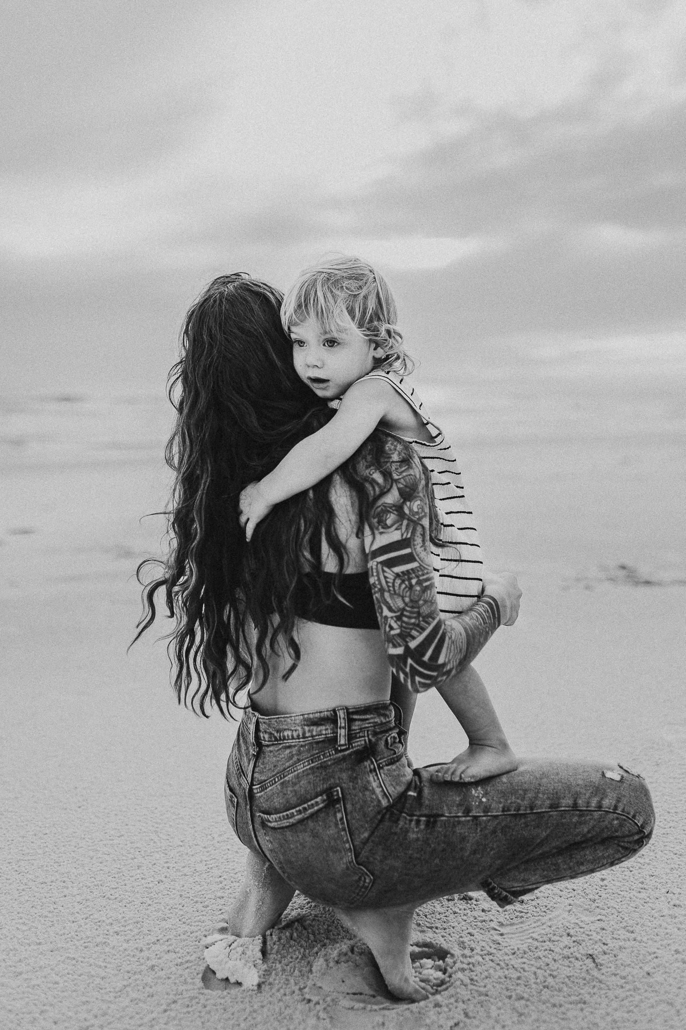 Tender black and white portrait series showing loving embrace between parent and child on a sandy beach destin Florida