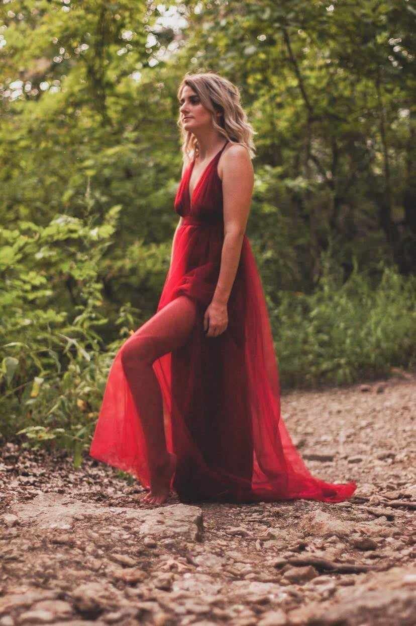 Artistic portrait of someone in a long red gown posing on a forest path.