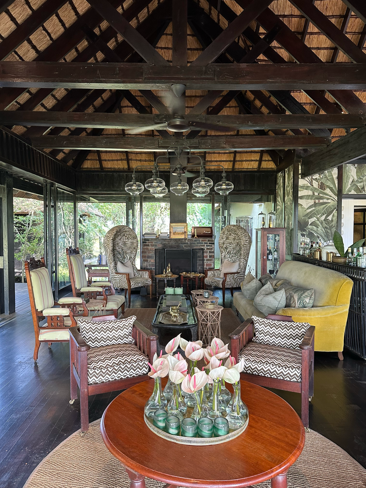 A luxurious safari lodge lounge with thatched roof, featuring comfortable seating and elegant decor with hanging light fixtures.