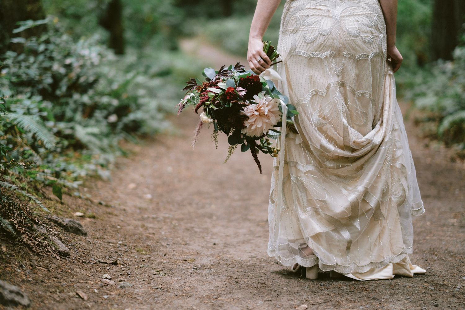 Bride in the pacific northwest holding a wedding bouquet at her side in one hand and wedding dress train in the other