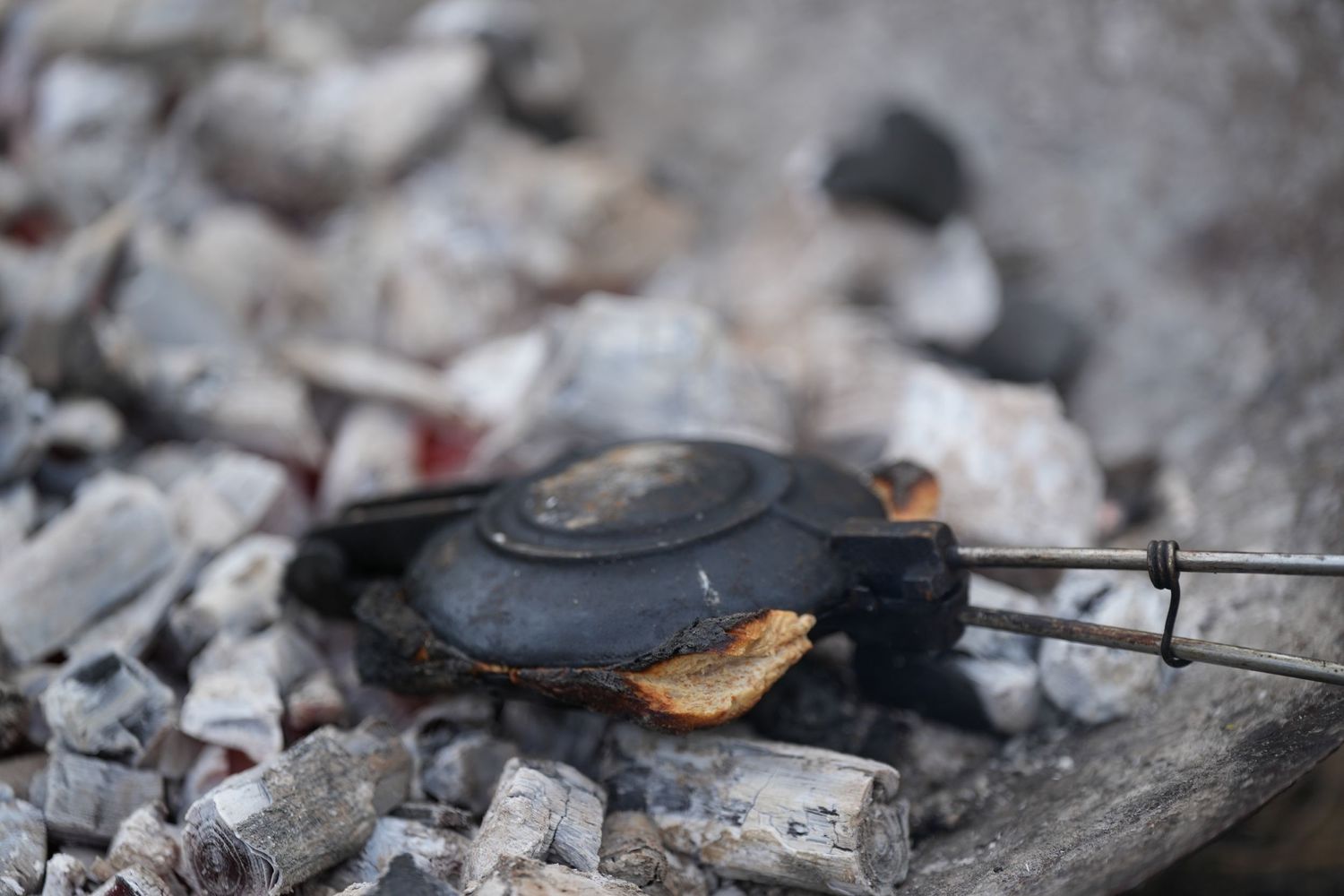 A rustic outdoor cooking setup showing bread being toasted over hot coals.