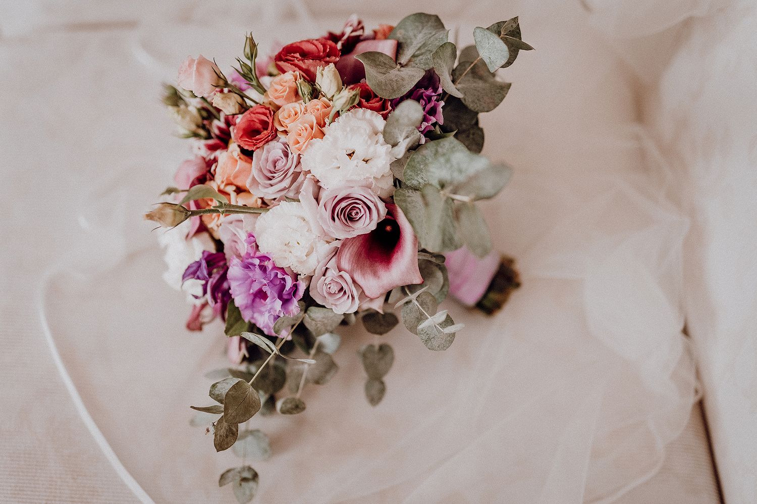 Elegant bridal bouquet with pink, purple, and white roses on white wedding dress fabric.