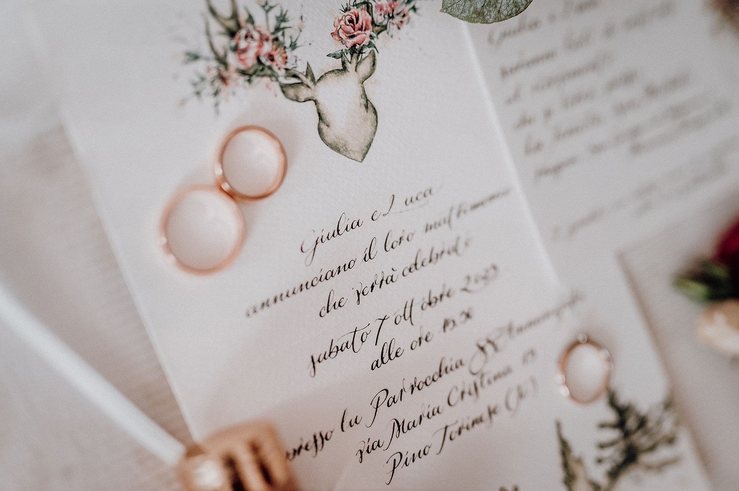 Close-up of wedding invitation featuring deer antler illustration with gold rings on white fabric.