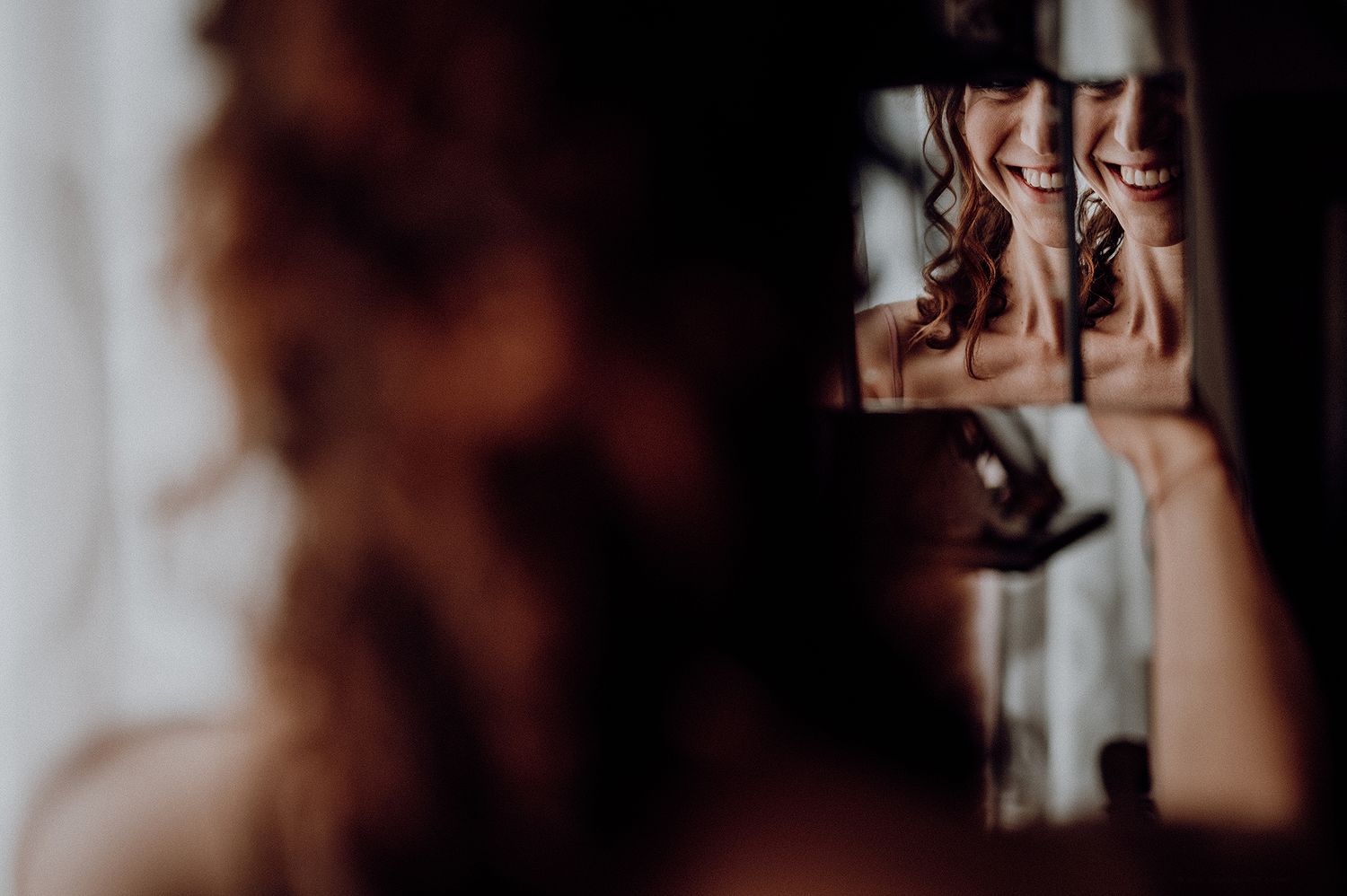 Smiling bride reflected in a handheld mirror fragment on her wedding day.