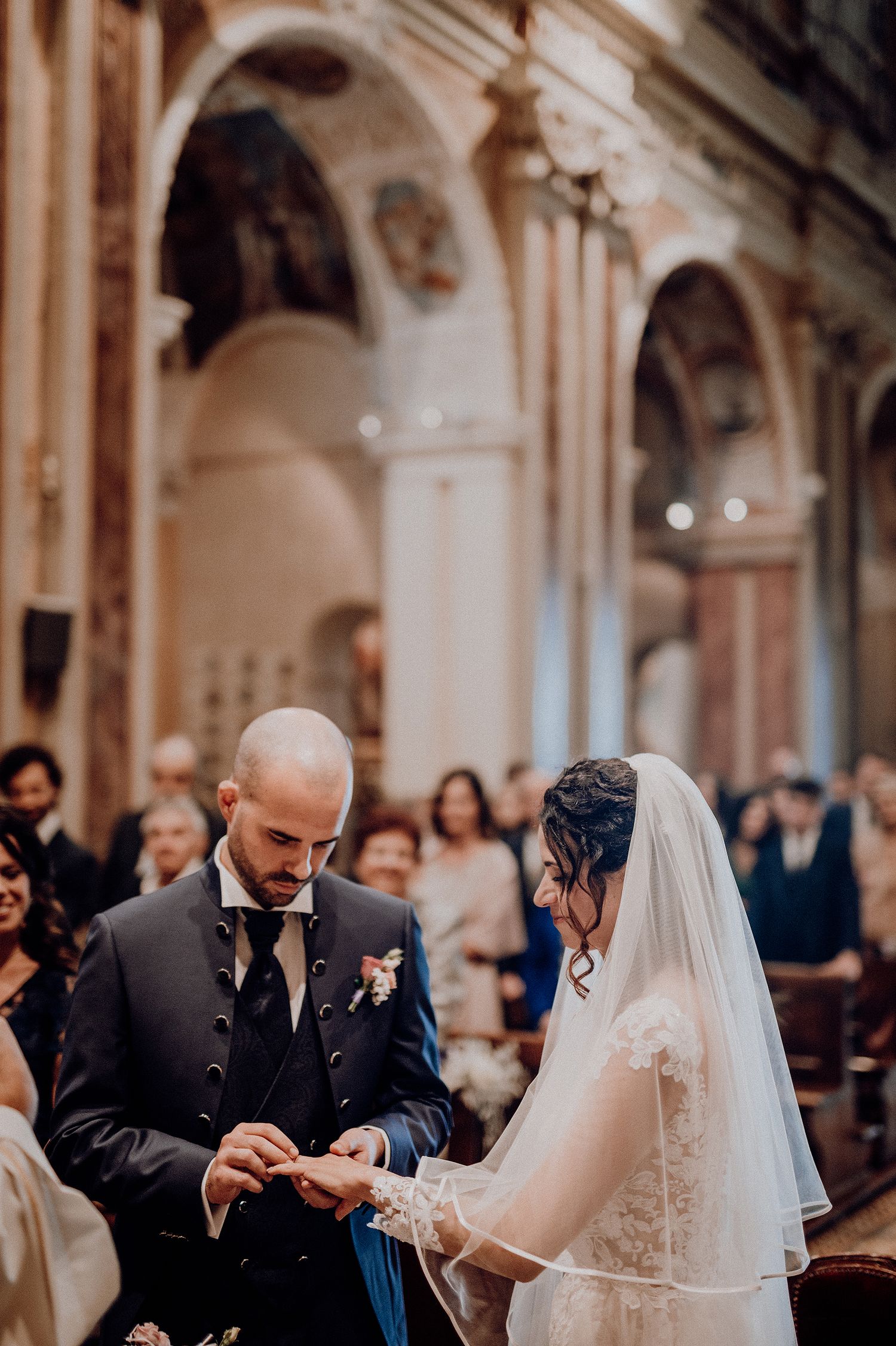 Groom places wedding ring on brides finger during ceremony inside an ornate Italian church.
