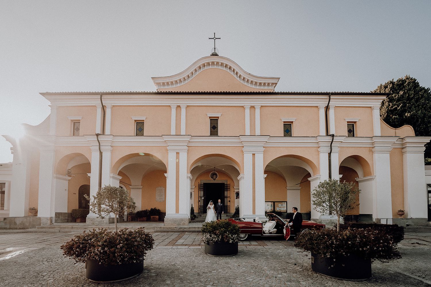 Bride and groom exit a beautiful neoclassical church with arched portico after ceremony.