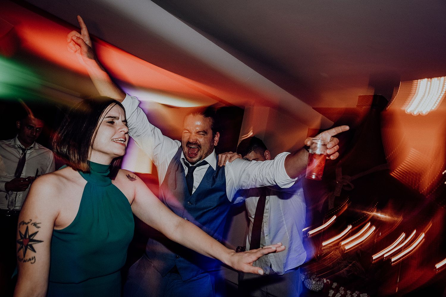 Wedding guests dancing energetically under colorful lights at a lively reception party.