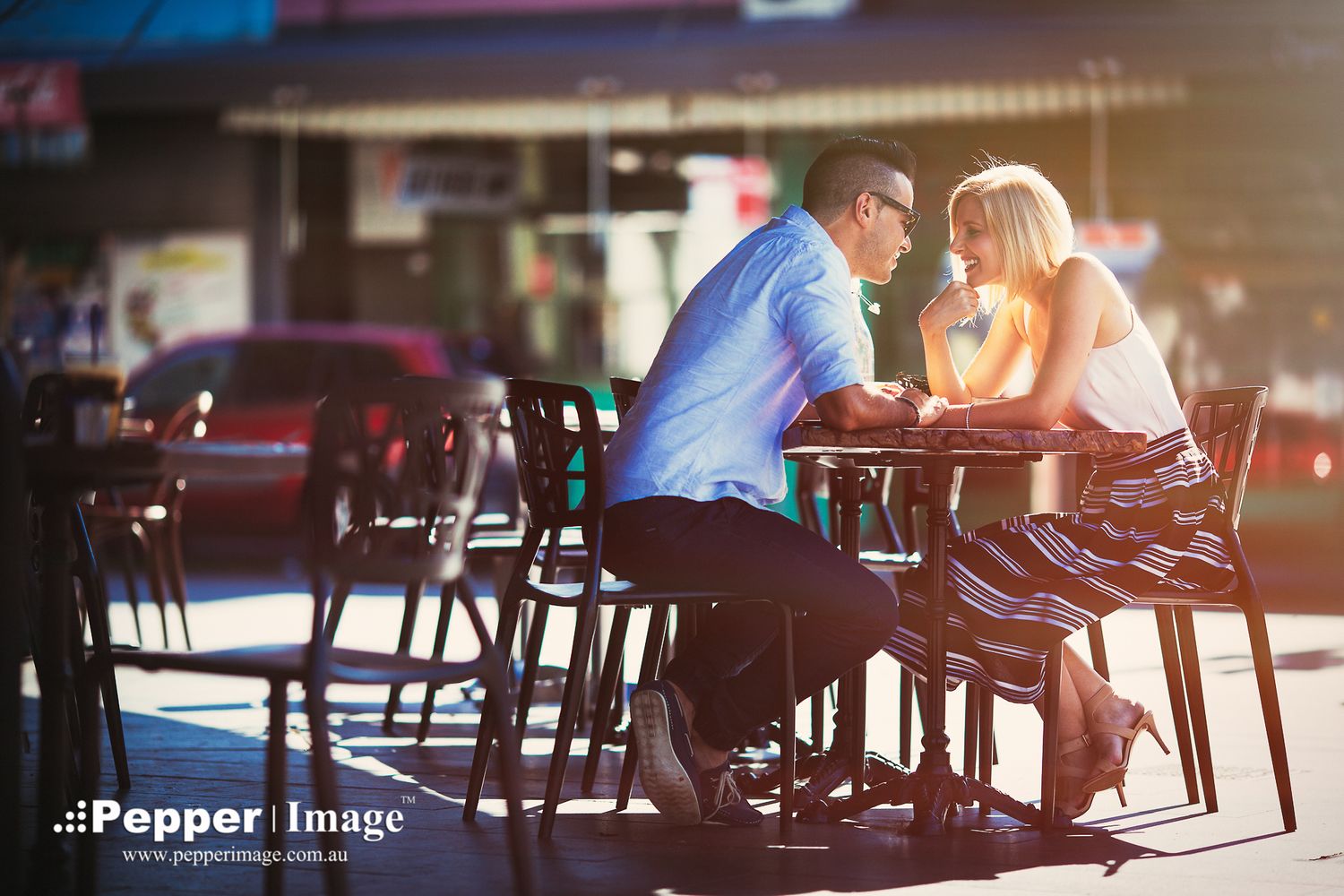 Romantic couple sitting close together at outdoor cafe table in warm sunlight.