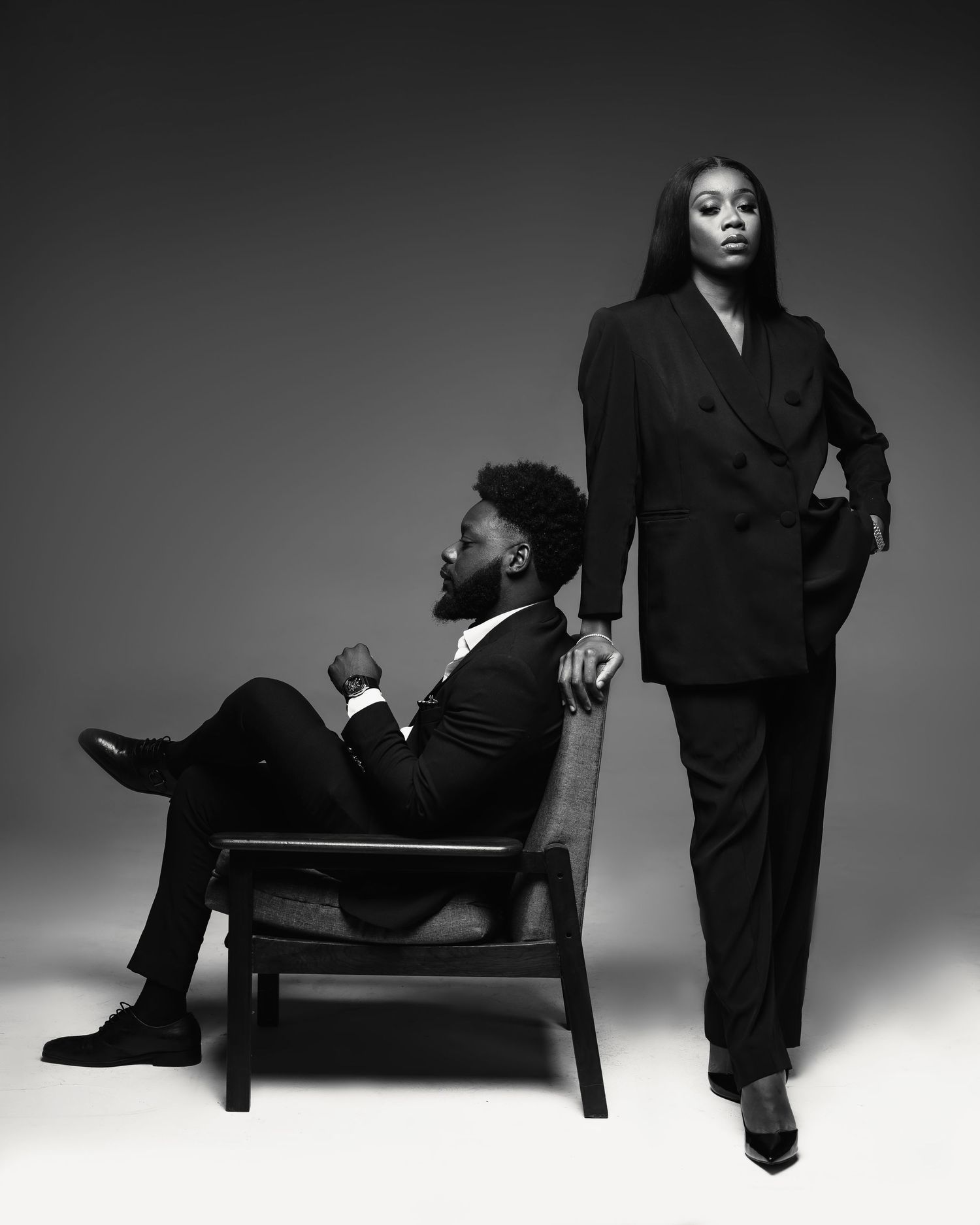 Artistic black and white fashion photograph featuring two people in elegant suits creating dramatic composition.