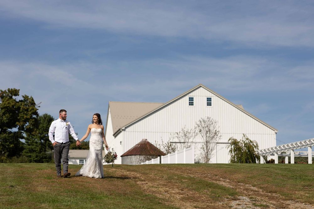 Couple stands in distance near white barn on rustic countryside property.