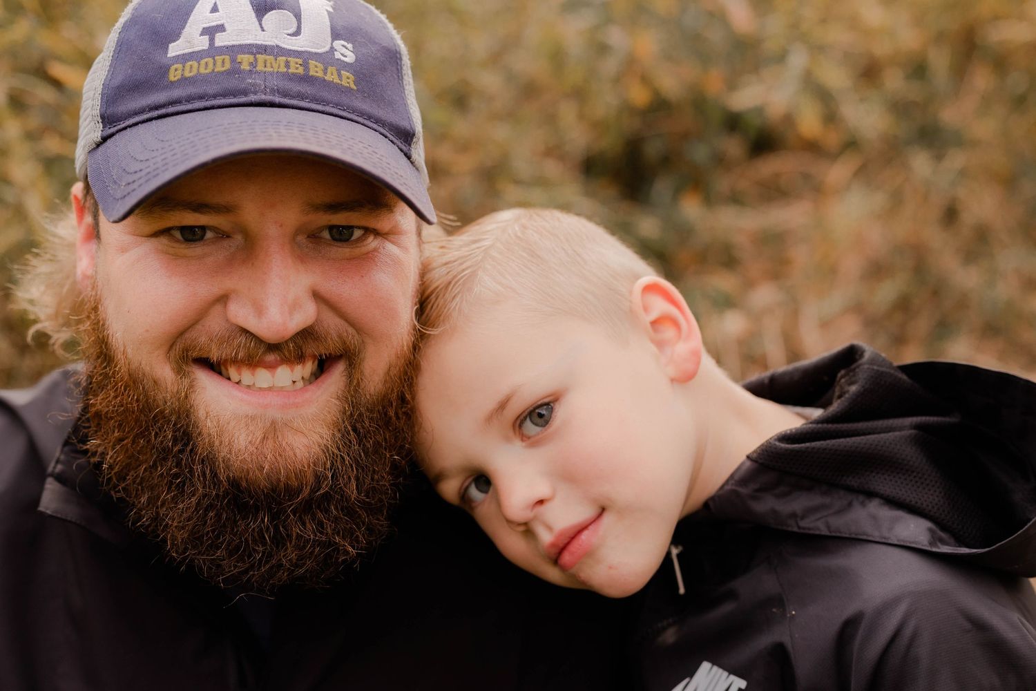 Sweet father-son moment captured in casual outdoor fall setting.
