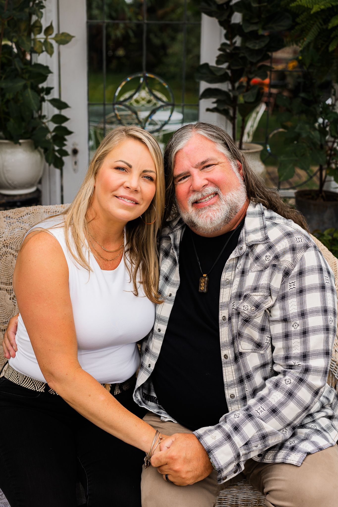 Cozy couple portrait session in greenhouse with white and plaid outfits.