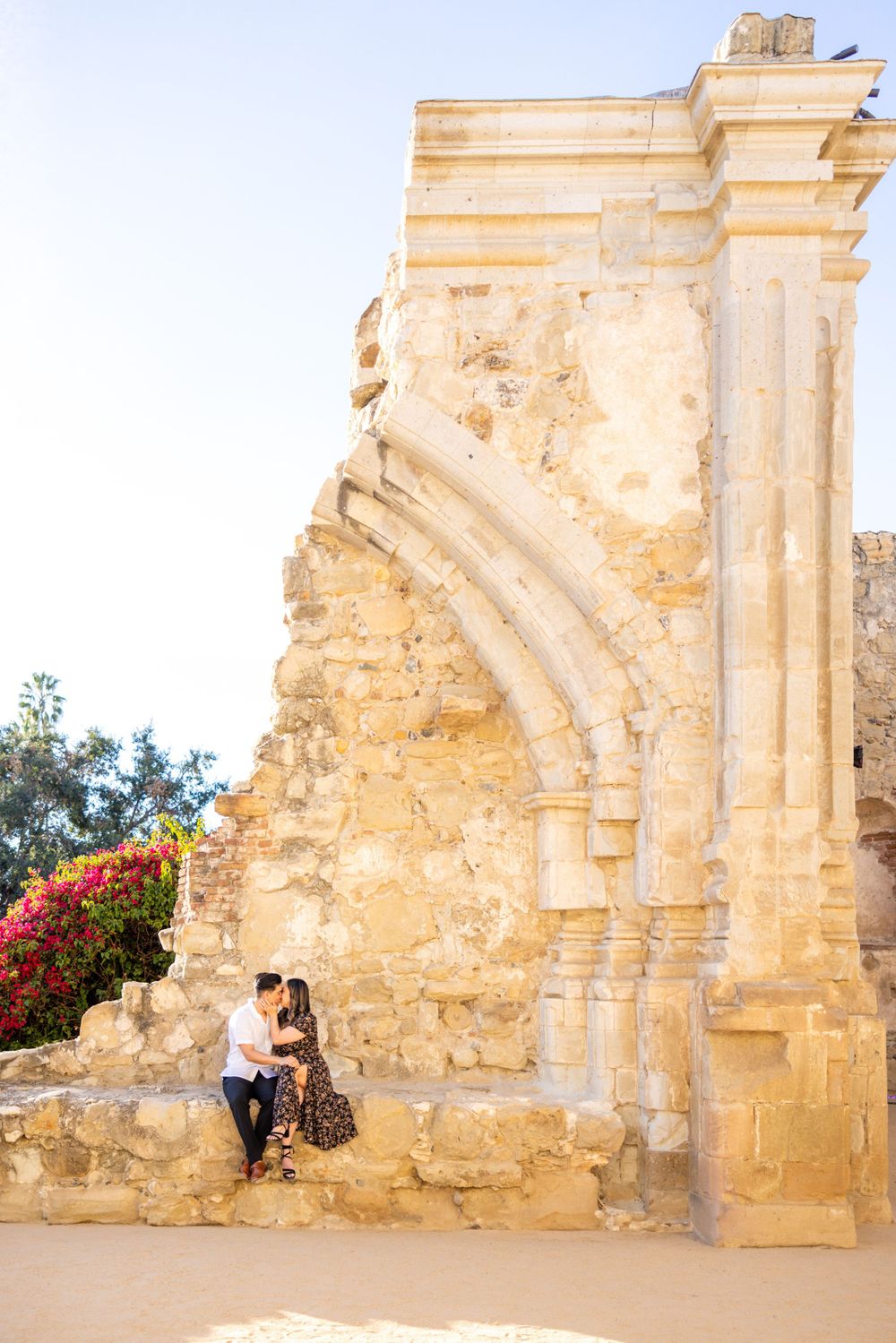 A couple shares an intimate moment while sitting on ancient stone ruins at sunset.