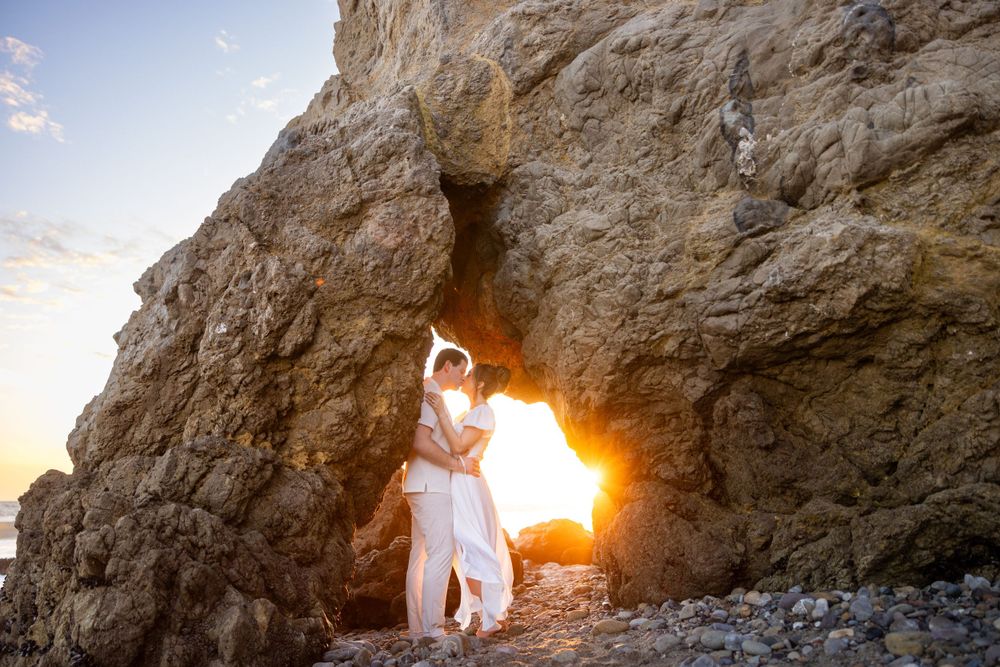 A couple poses in a sea cave with sunlight creating a stunning natural frame.