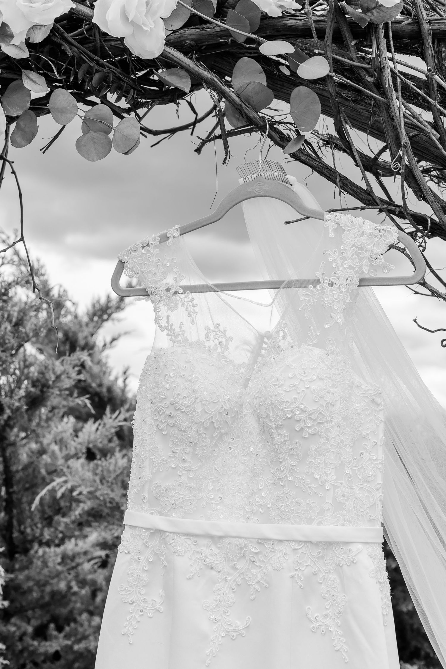 A delicate white lace wedding dress hangs against a dark background.