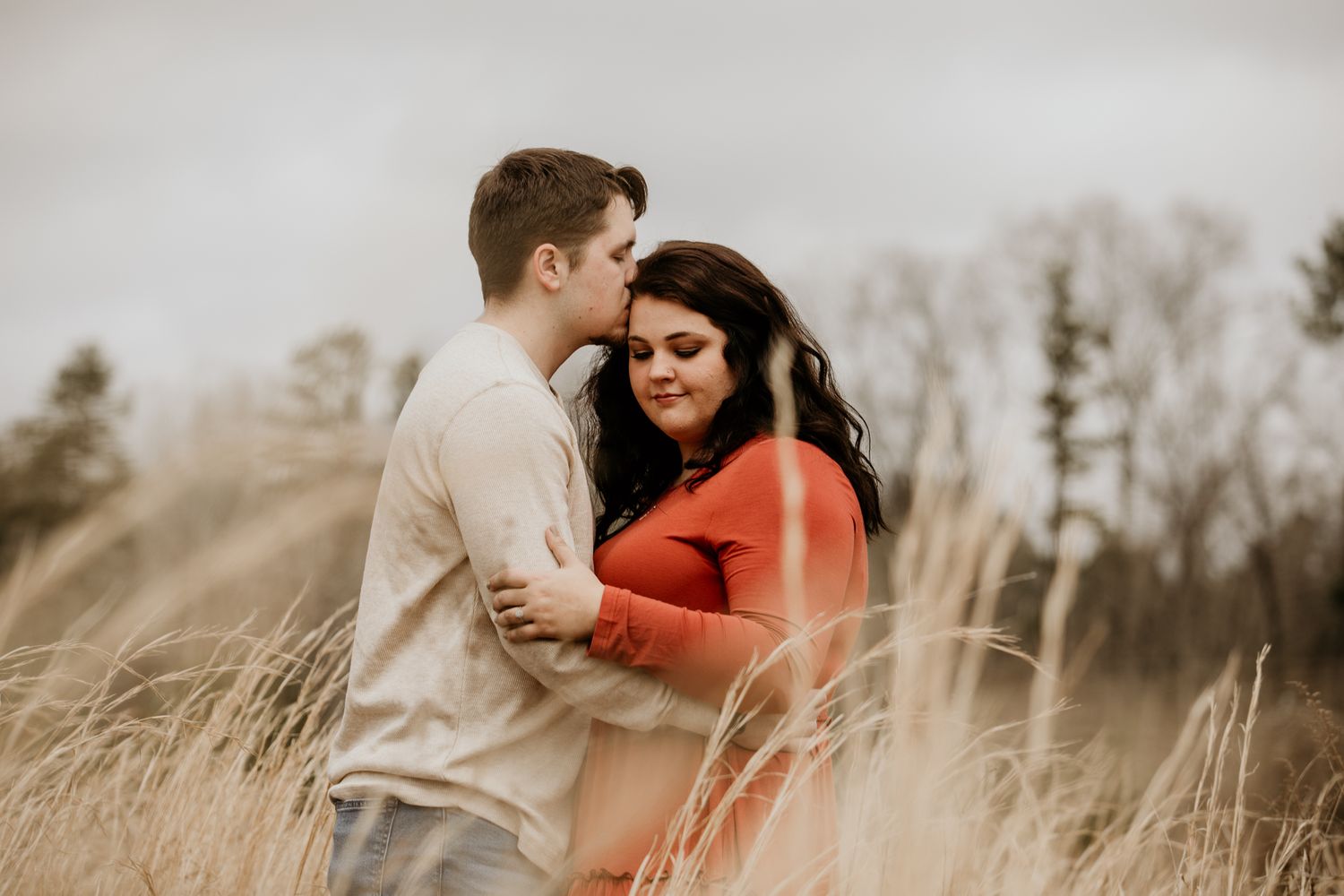 A couple embraces intimately in a field of tall grass during golden hour.
