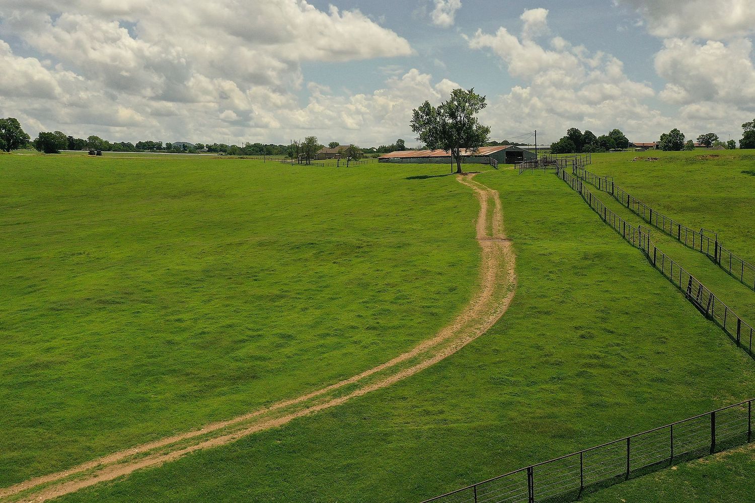 A dirt pathway leading to an old country barn cuts through lush, green pastures.