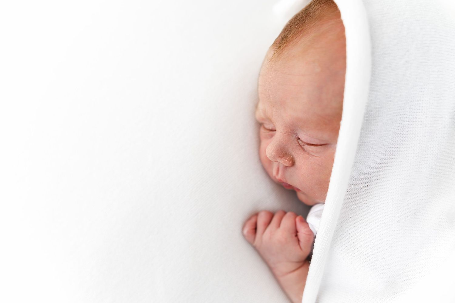 Sleeping newborn baby wrapped in soft white blanket during peaceful slumber.