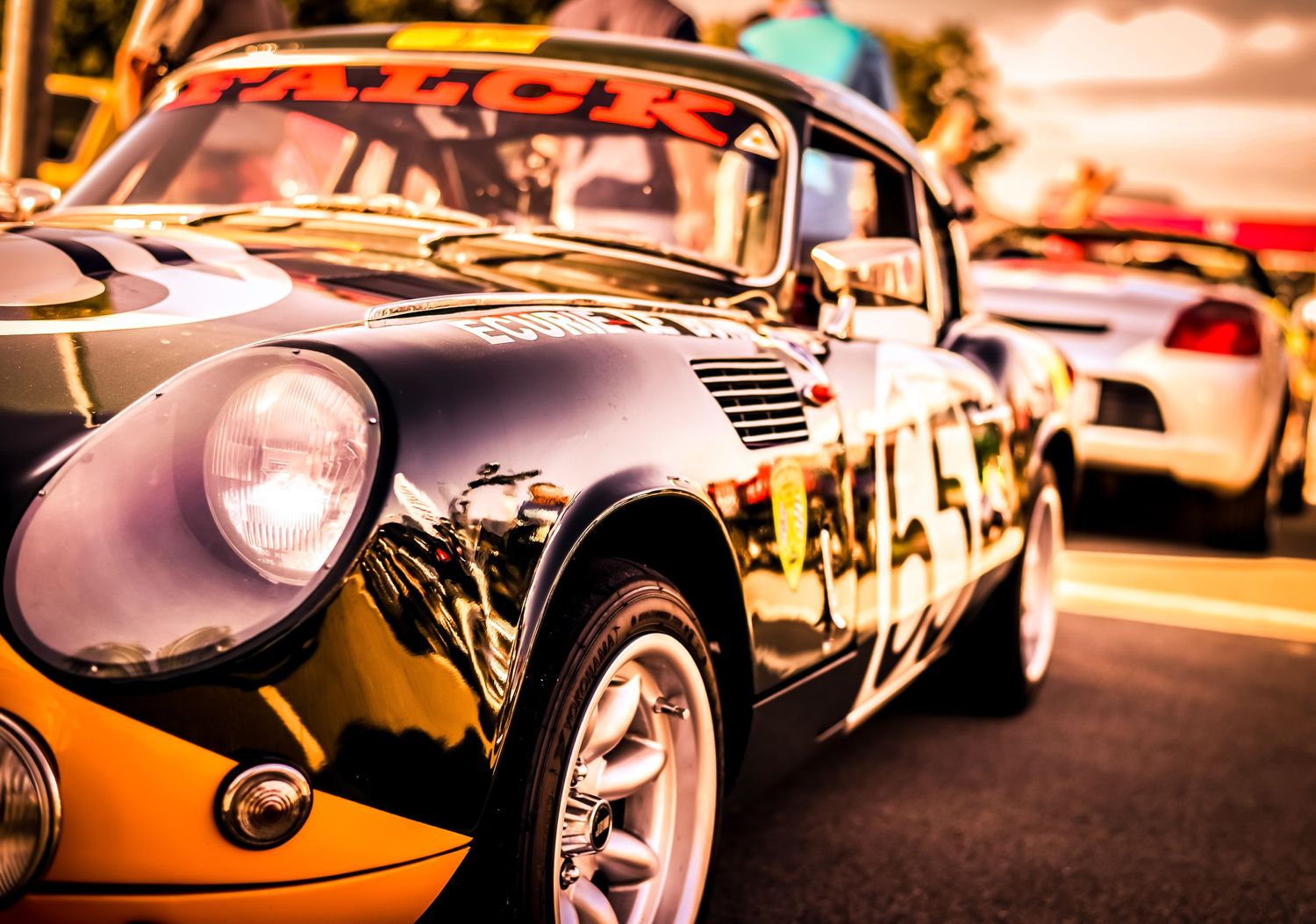 Vintage black classic car with chrome details and round headlights parked at a car show in warm sunset lighting.