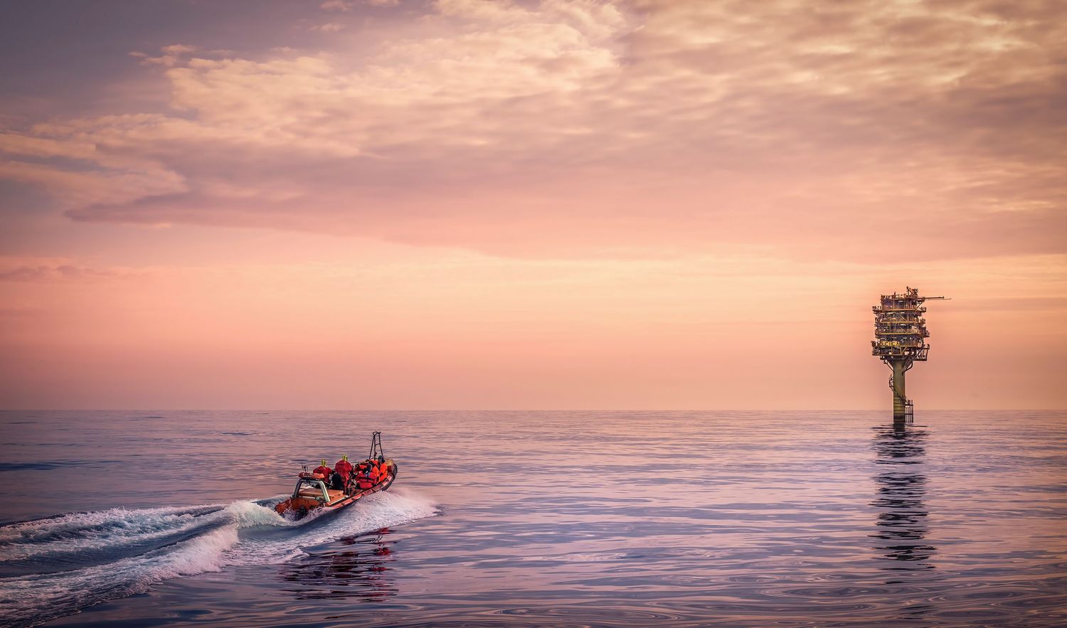 Silhouetted boats and ships on calm ocean waters against vibrant orange and purple sunset skies.