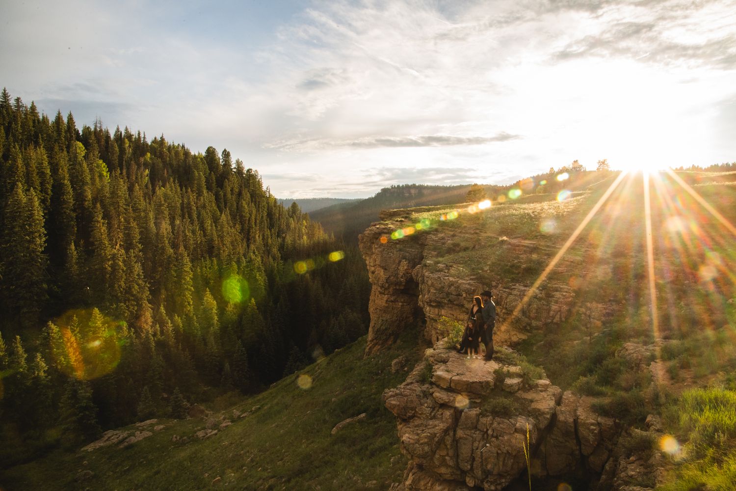 Mother Father and two young daughters dressed up and standing on a cliff overlooking a river