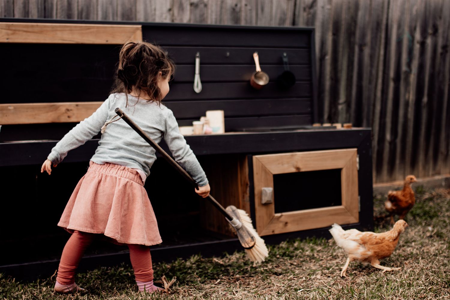 Toddler Isla chasing chicken with a broom documentary style photo