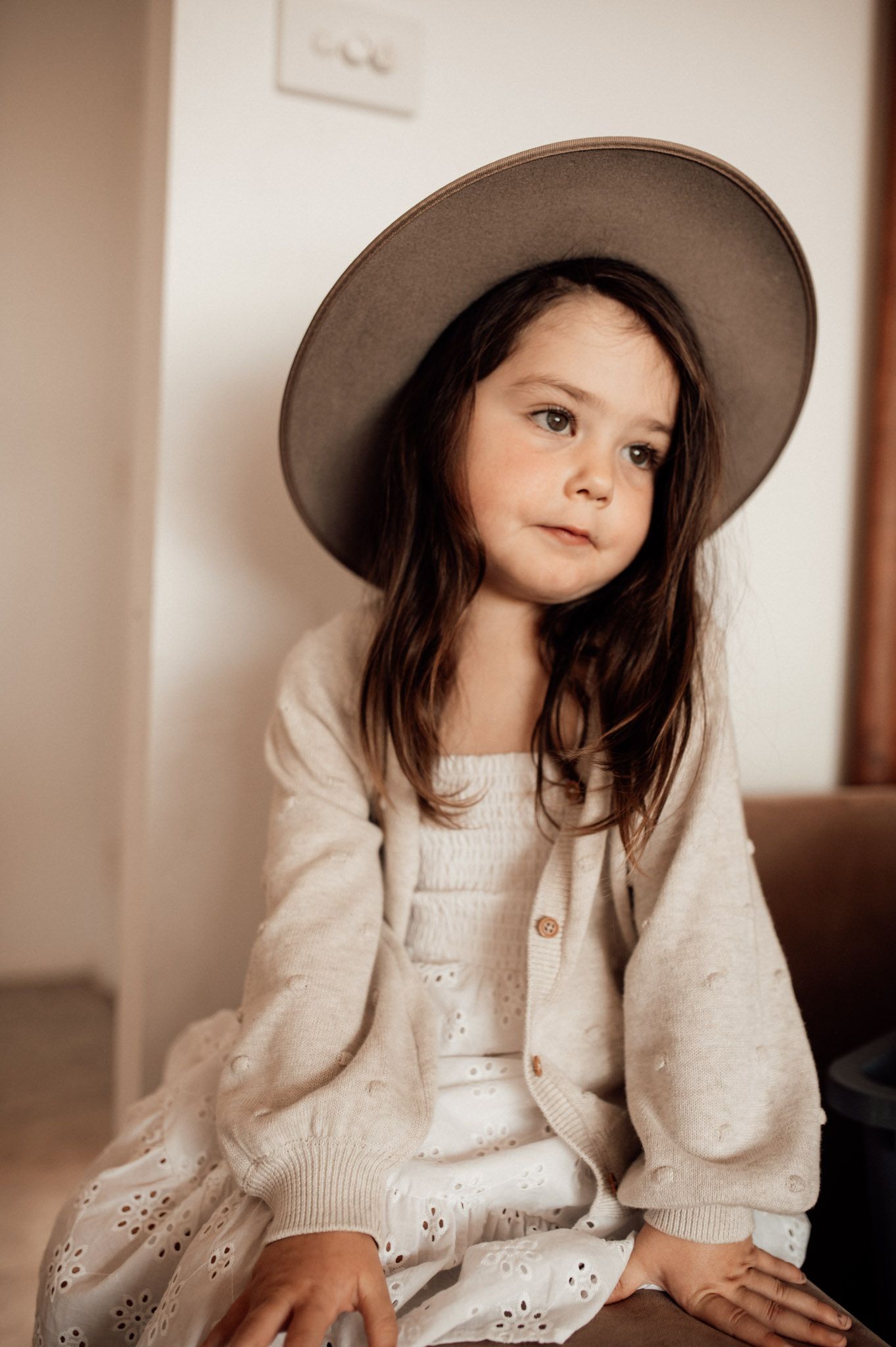 Young girl in cowboy hat looking out the window wearing white dress