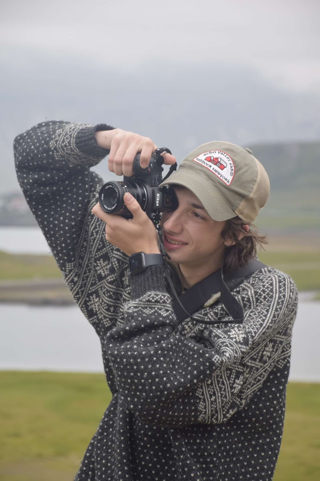 A photographer wearing a patterned sweater and cap takes photos in nature.