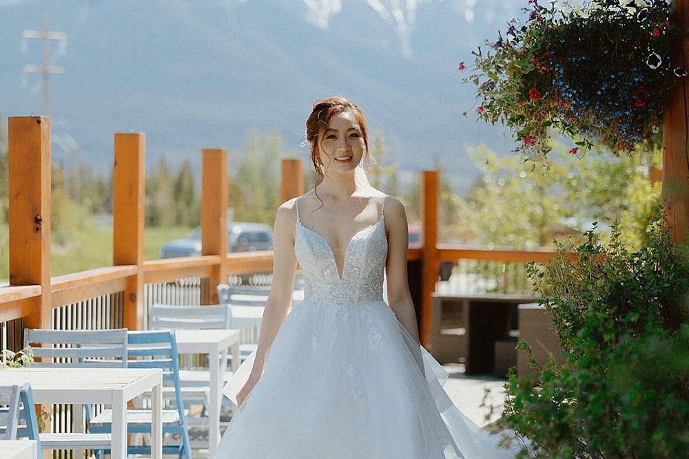 A wedding dress featuring intricate lace details and a plunging neckline against a mountain backdrop on a sunny day.