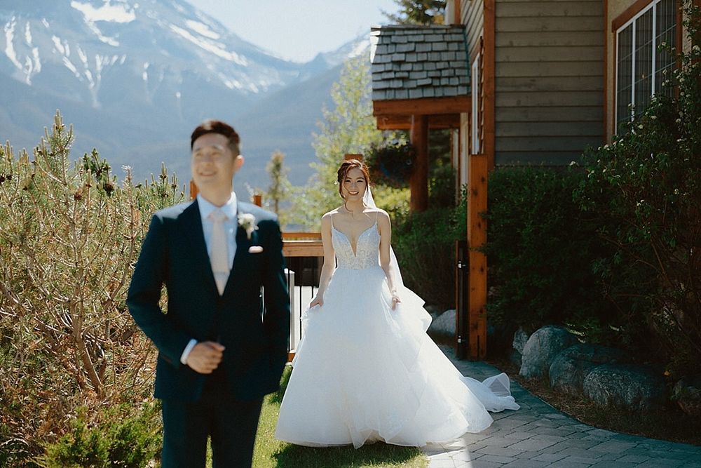 A couple in wedding attire walks together on a mountain path with snow-capped peaks in the background.